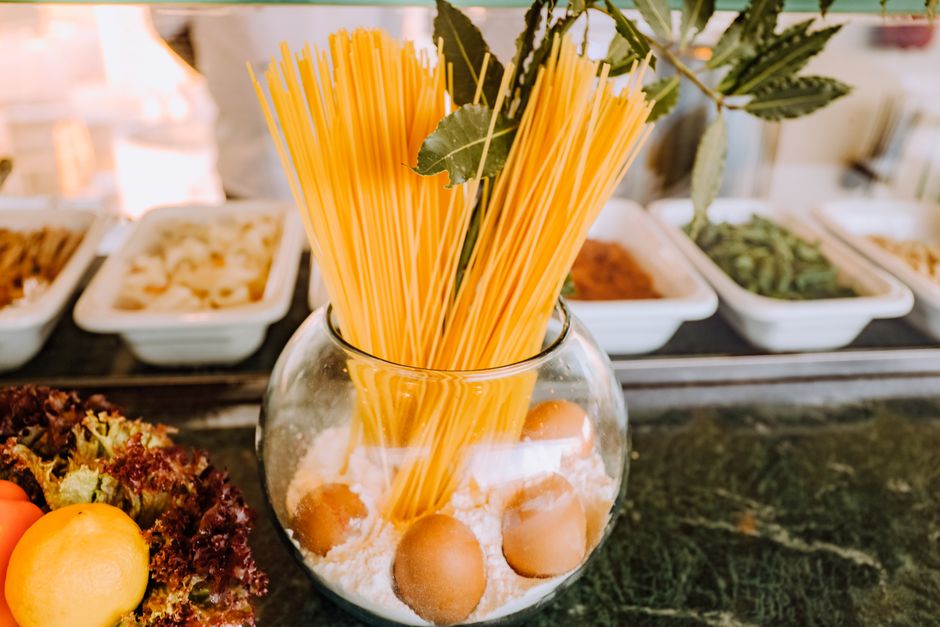 A creative arrangement of spaghetti, eggs, and flour in a glass bowl with vegetables.