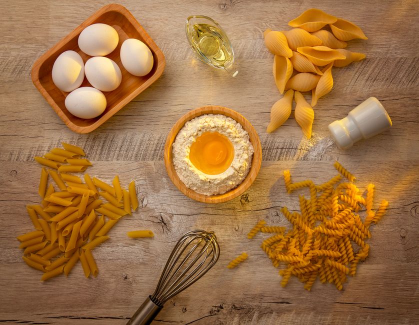 Aerial view of pasta ingredients including eggs, flour, and oil on a wooden table.