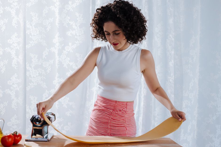 Woman making fresh pasta at home using a pasta roller, highlighting traditional Italian cuisine methods.